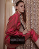 Woman wearing black lizard embossed calfskin leather cross-body box bag with large buckled belt across front, silver hardware
