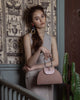 Woman carrying dusty rose calfskin and suede leather, half moon silhouette handbag with cellulose acetate top handle.
