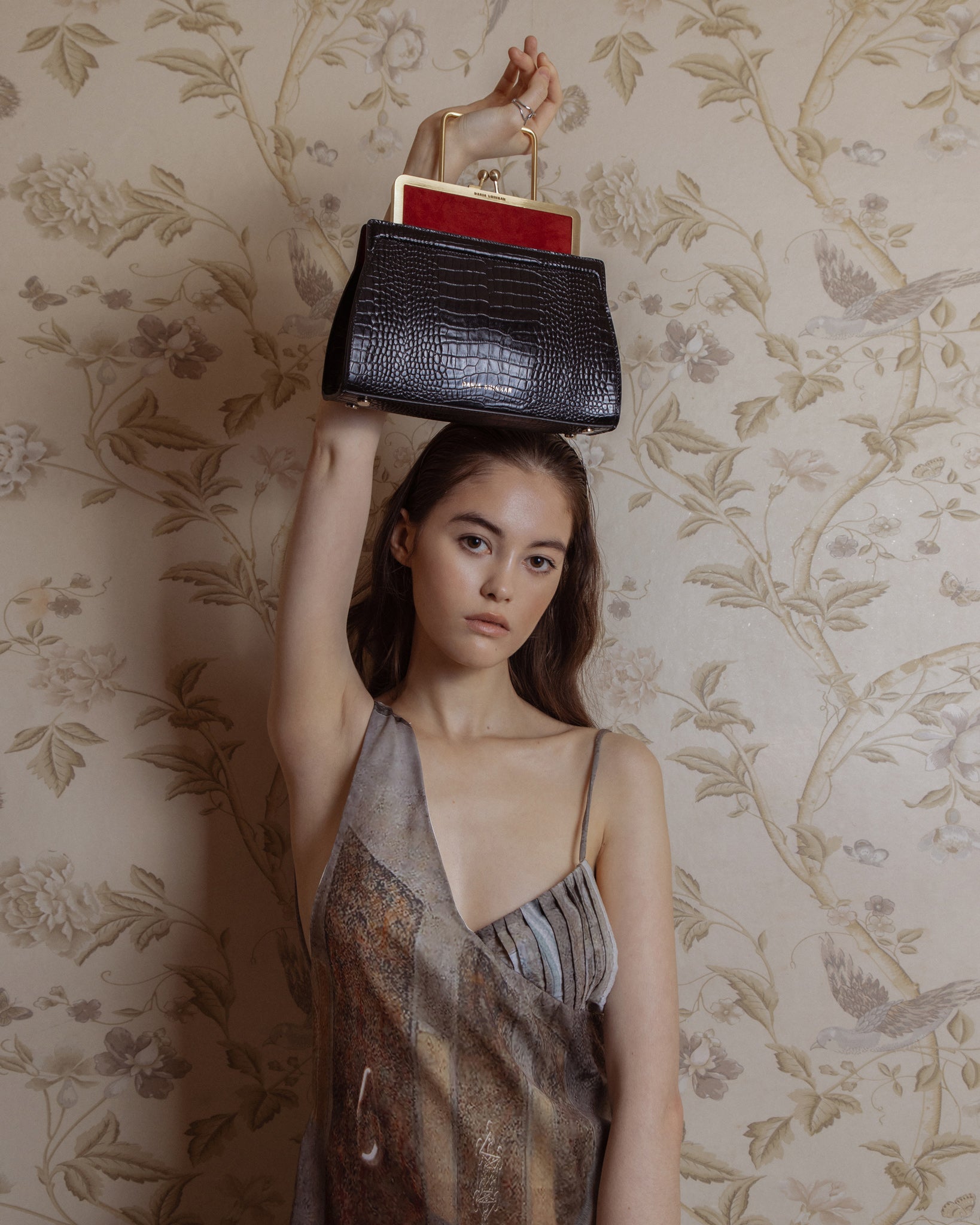 Woman carrying black crocodile embossed calfskin, ruby red suede leather handbag, with brass frame in light gold finishing.